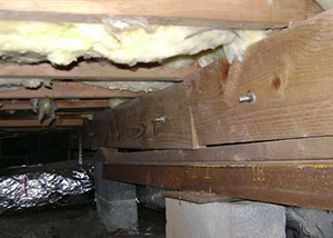 A sagging crawl space with concrete supports and wooden shimming a Milaca crawl space